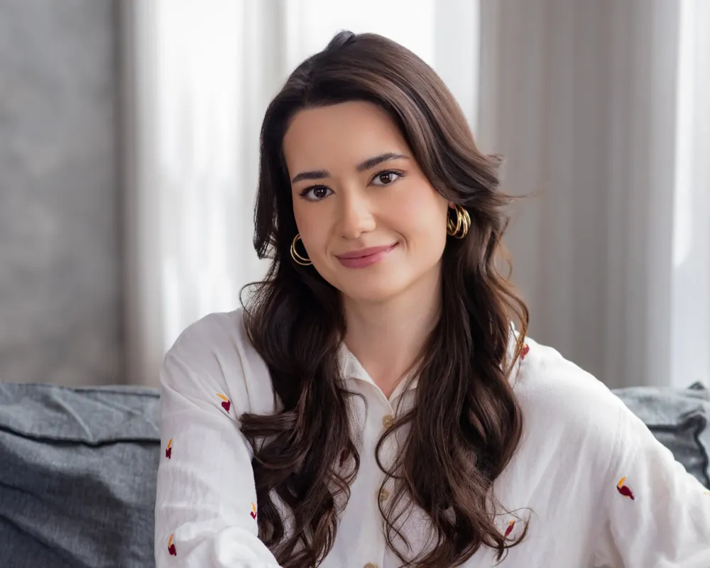Isabela Matoso sentada no sofá, olhando para a câmera